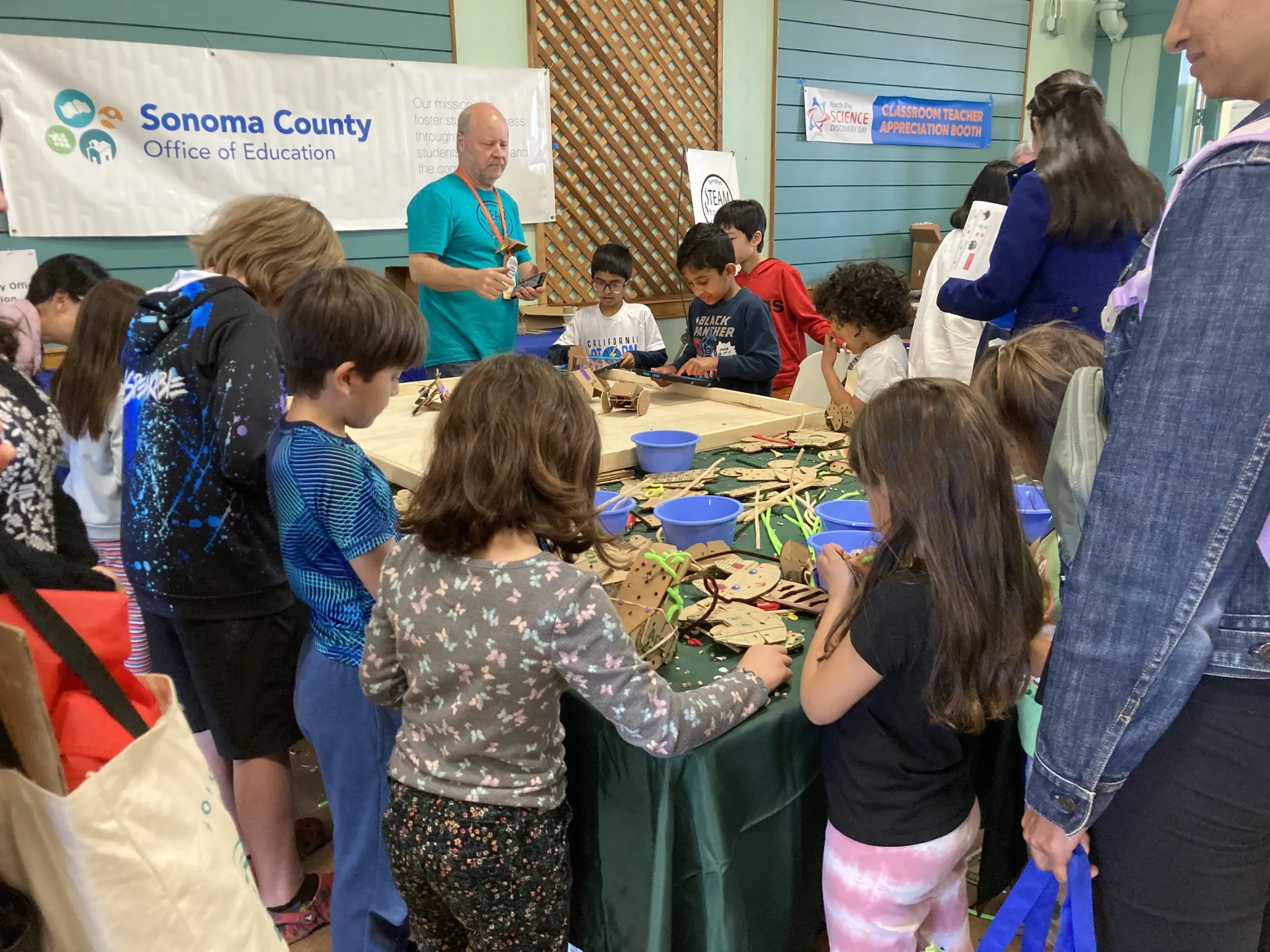 Kids gather around a table covered in cardboard parts and connectors.