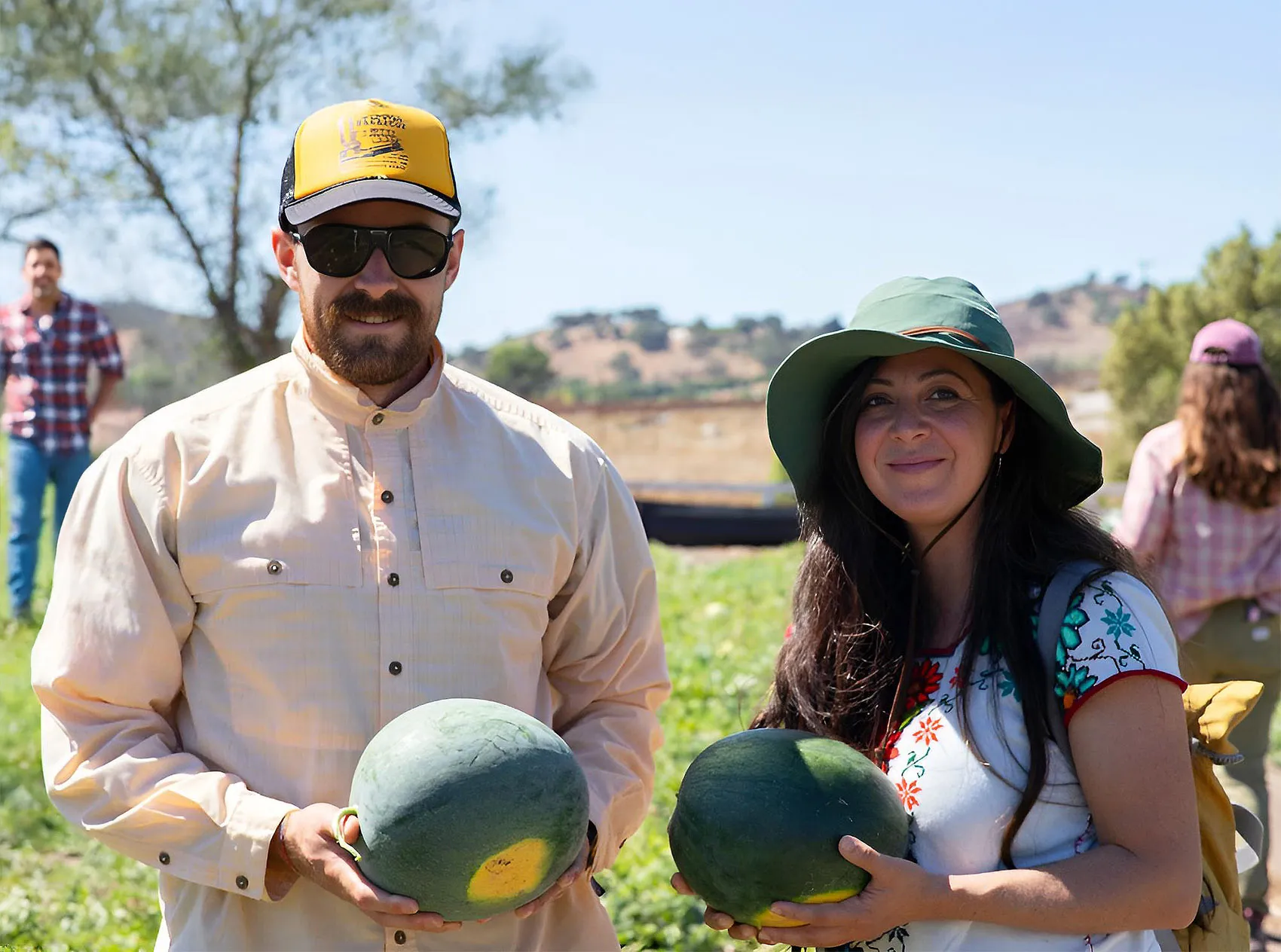Two farm advisors holding watermelons in a field