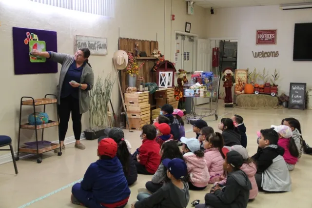 Woman stands in front of a group of children, teaching them how to create healthy meals.