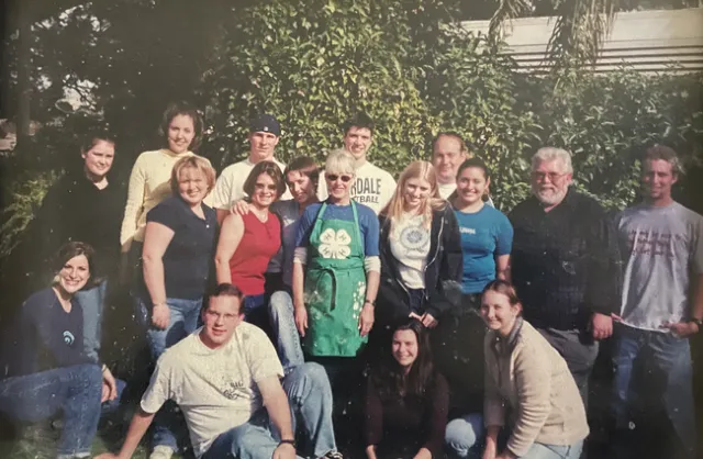 A group of teenagers surrounding an older woman and man while smiling at a camera.