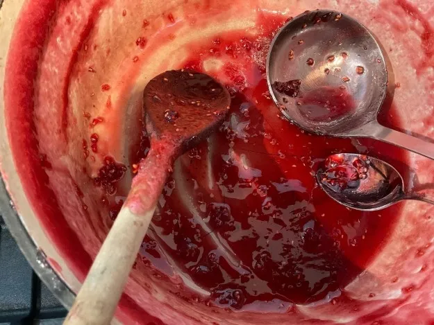 Bottom of the jam pot with leftover jam and three spoons resting inside.