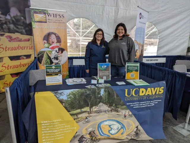 Two women pose beside a banner of red strawberries and another banner that reads: 