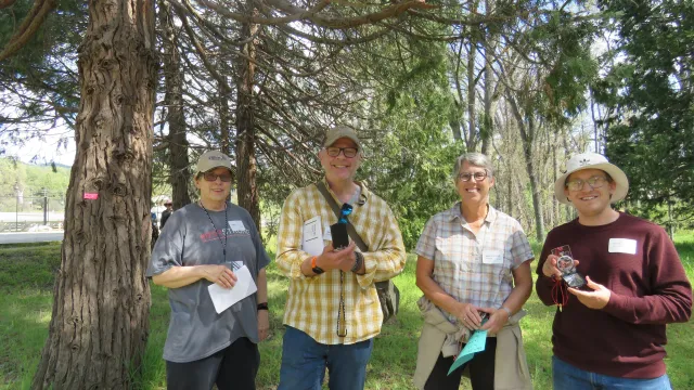 Four people stand in a forest and hold up compasses.