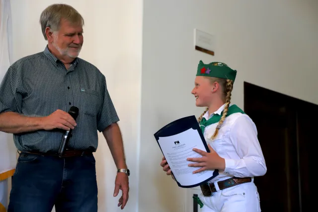 A girl in a 4-H uniform receives an award from a man on stage.