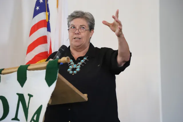 A women speaks at a podium with the American flag behind her.