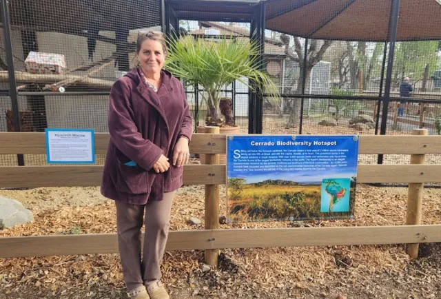 Woman in burgundy coat with glasses on top of her head poses by the fence of a zoo enclosure where she did habitat design