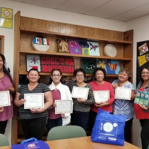 Seven adults hold their EFNEP graduation certificates along with the nutrition educator.
