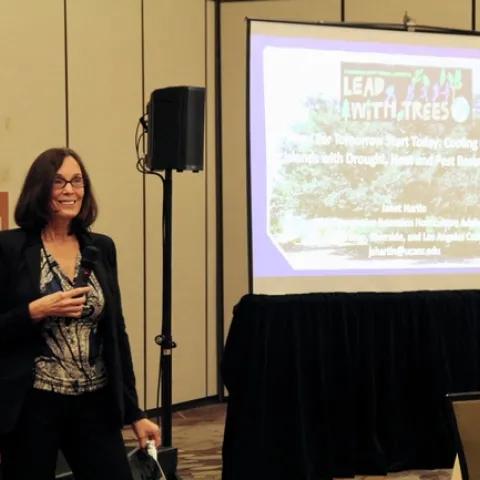 Janet Hartin is standing in front of a powerpoint presentation that displays her research.