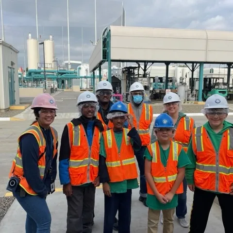A group of young students posing in front of a water recycling facility with their tour guide.