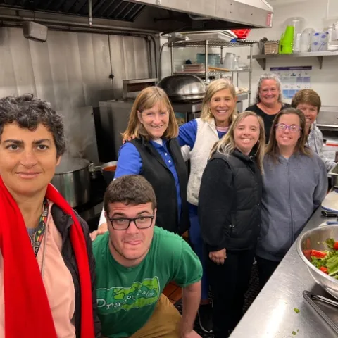 A group of people smiling at the camera while standing in a kitchen, preparing food.