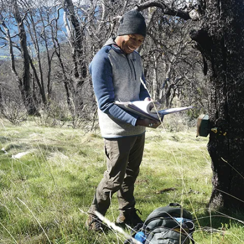 Surrounded by green grass, a man wearing knit cap and long-sleeved sweatshirt pages through a binder