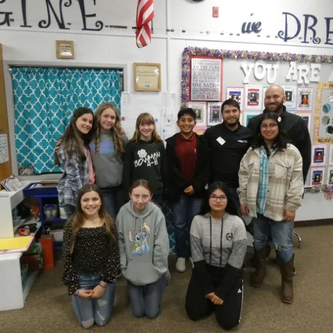 A group of sixth graders stand with educators in a classroom