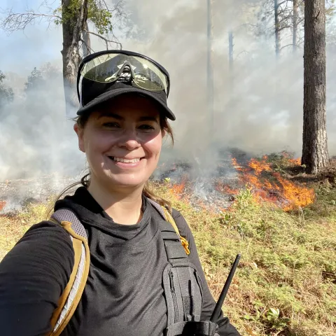 Woman smiling at the camera and standing in the forest.