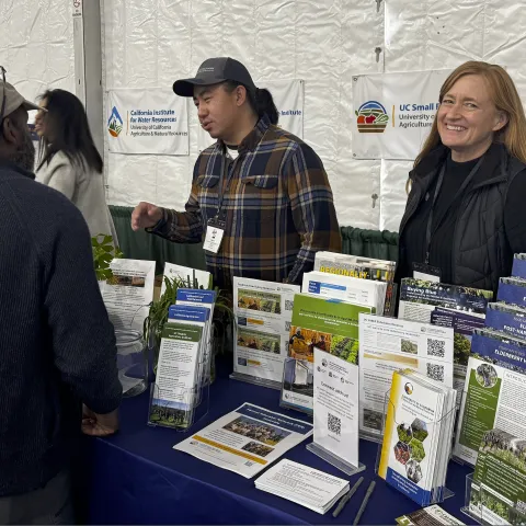 Two UC ANR representatives speak with an attendee during the EcoFarm 2026 conference.