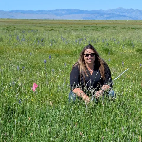 Tracy crouches in a field surrounded by green pasture