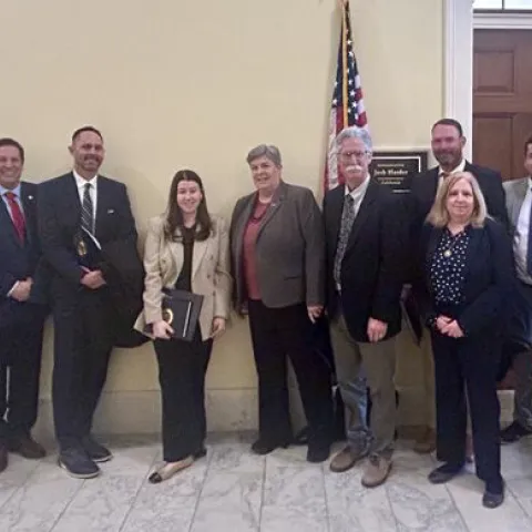 Ten people wearing business suits stand in front of U.S. flag
