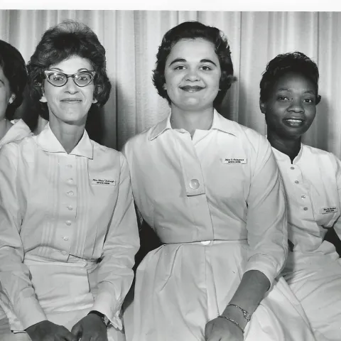 Three white women and one Black woman wearing white uniforms