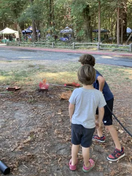 A boy observes as another boy aims a water hose stream at wood cutouts of "flames."