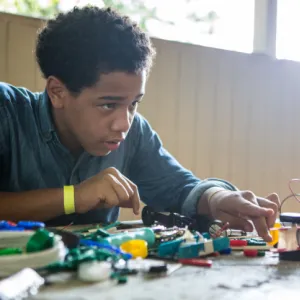 A seated teenager is shown working on lego robotics construction
